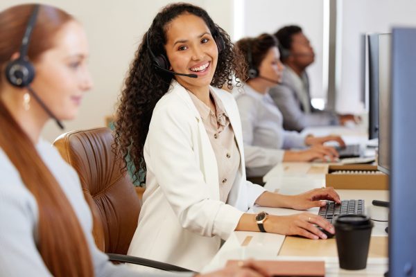 Portrait of a young call centre agent working on a computer alongside her colleagues in an office.