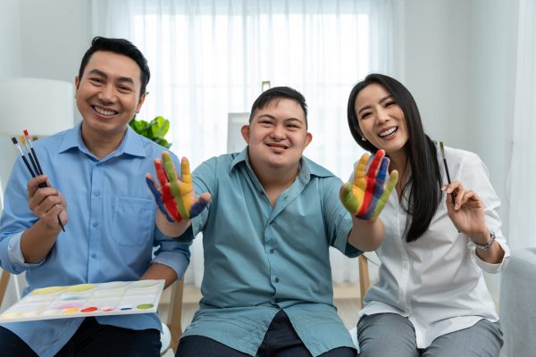 Portrait of Asian happy family, parents draw picture with young son. Beautiful loving couple, mother and father take care and teach young man painting artwork indoors and looking at camera in house.