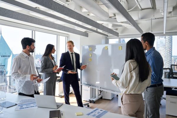 Busy professional diverse team business people coworkers working on corporate strategy in office meeting room. International company workers group having whiteboard presentation and discussion.